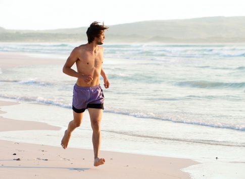 A man in a swimsuit running along a beach.